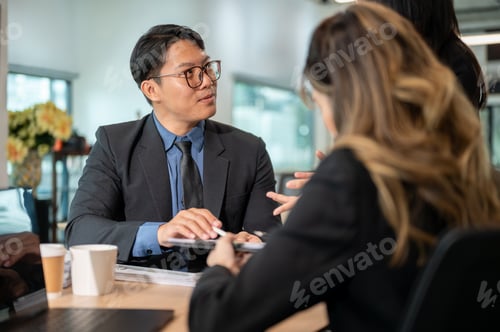 Preview: Back view of businesswoman and glasses man looking at coworker while sits at wooden table in office.