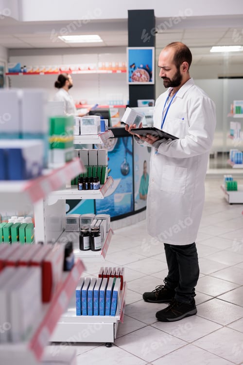 Preview: Pharmacist looking at pills packages typing inventory information on tablet computer