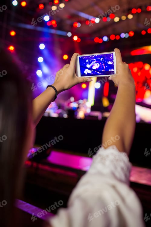 Preview: Young woman taking photos with smart phone at music festival