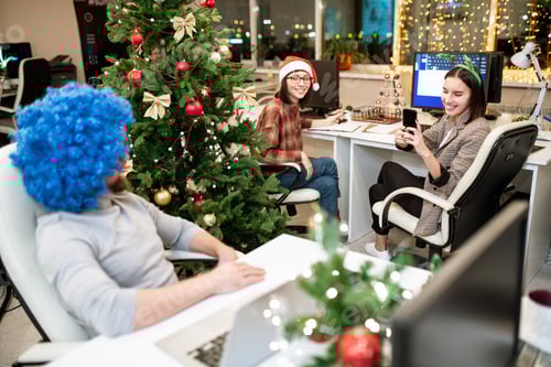Preview: One of young happy businesswomen taking photo of colleague in blue wig
