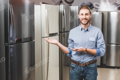 Preview: smiling consultant pointing with hands at fridge in home appliance store