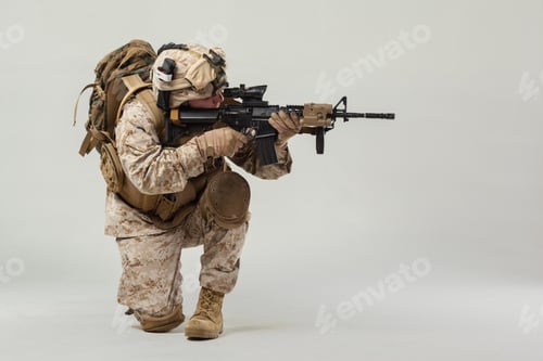 Preview: Soldier in uniform kneeling with weapon in a studio against a plain background