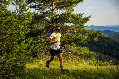 Preview: Caucasian man running through a scenic forest trail with mountains in the background in the morning
