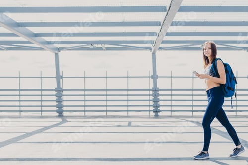 Preview: Positive slim fitness girl going on training, being photographed in motions, carries bag.