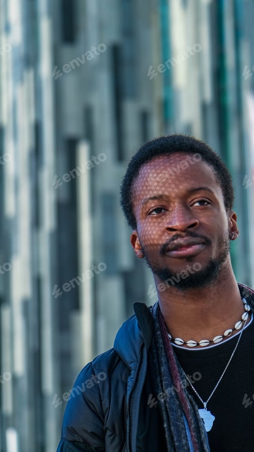 Vista previa: Young African man in a black outfit walking in a street posing in front of a glass paneled building