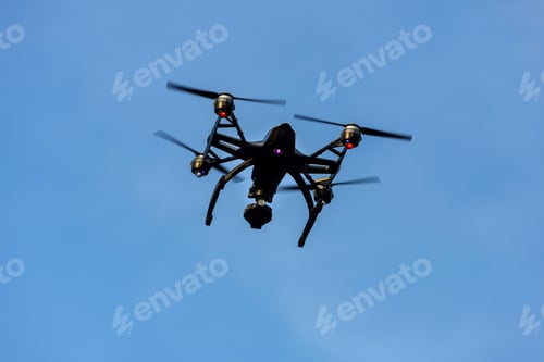 Preview: Black drone quadcopter with camera flying over blue sky angle view, copy space.
