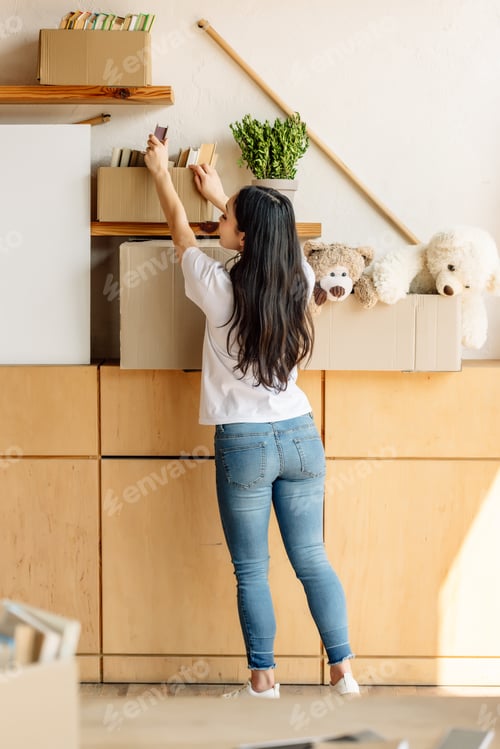 Preview: back view of young volunteer girl getting books from carton box