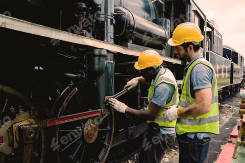 Preview: Two men in yellow helmets are working on a train engine. One of them is holding a wrench