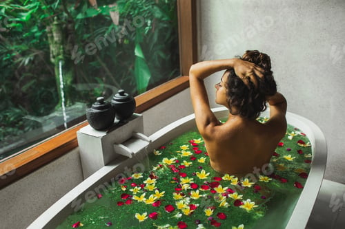 Preview: Beautiful young woman enjoying in spa, view from behind. Luxury stone bath tub with jungle view