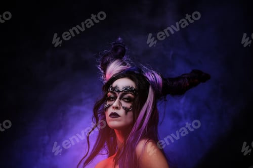 Preview: Young woman wearing banshee dark make-up and violet horns posing in a studio with smke