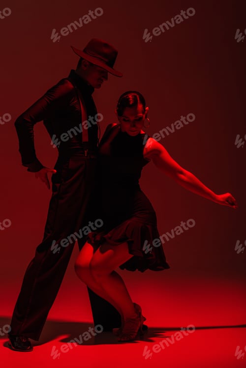 Preview: passionate couple of dancers in black clothing performing tango on dark background with red