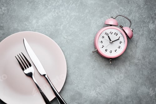 Preview: Alarm clock and plate with cutlery. Concept of intermittent fasting, lunchtime, diet and weight loss