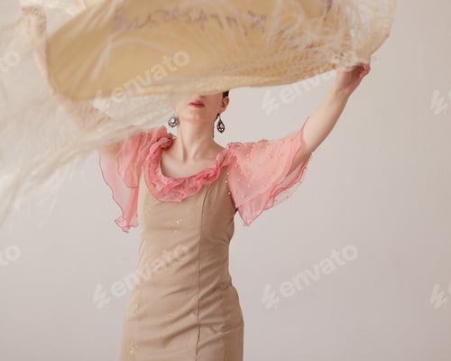 Preview: Beautiful young woman in pink, beige dress dancing flamenco with shawl.Scarf flutters in her hands
