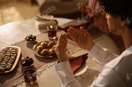 Preview: Close up of Muslim man and his wife praying together at dining table.