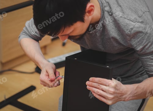 Preview: A young man tightens a screw with a figured wrench on black shelves.