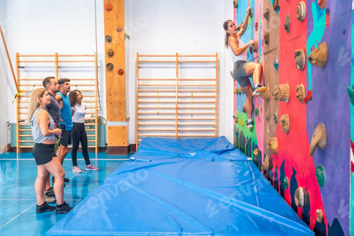 Preview: Determined sportswoman climbing wall with friends watching in gym