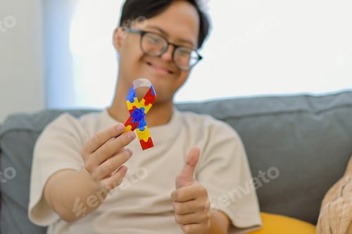 Preview: Young Man Showing Autism Awareness Ribbon with Thumbs While Sitting on Sofa