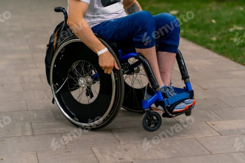 Preview: Portrait of a young man with a disability in a wheelchair in a city park against background of trees