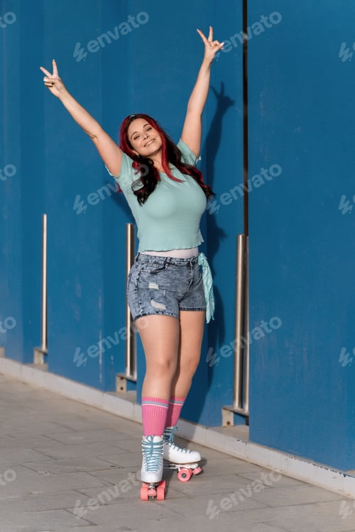 Preview: Redheaded roller skater smiling with her arms up in the air doing the victory sign.