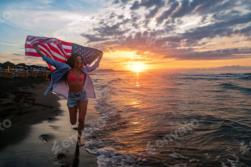 Preview: Happy woman smiling and running on beach with the US flag. July 4th independence day. Holiday