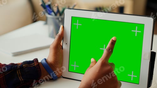Preview: Young worker looking at horizontal greenscreen display on tablet