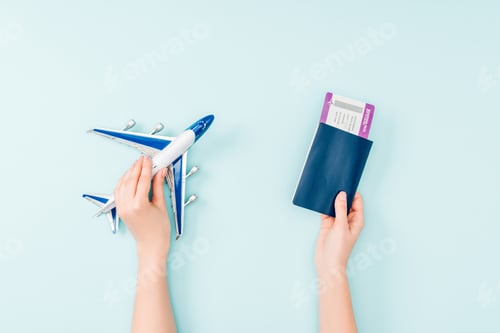 Preview: cropped view of woman holding passport, air ticket and toy plane on blue background