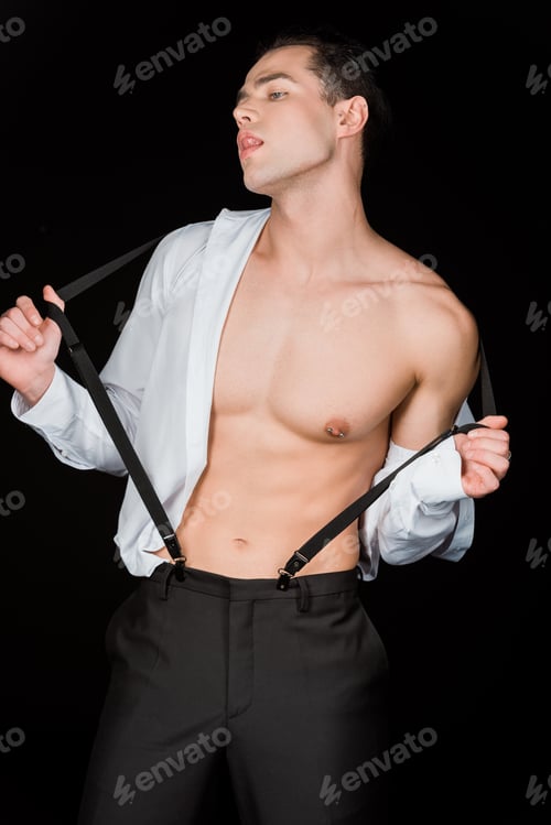 Preview: handsome man showing tongue while touching suspenders isolated on black