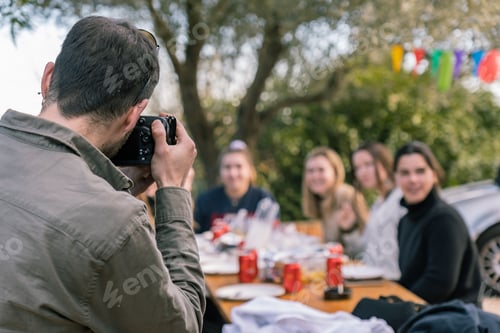 Preview: Young man taking a picture of girls sitting at the table during a birthday party with a camera