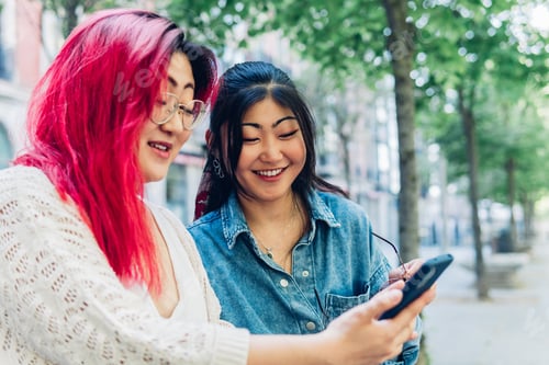 Preview: Smiling Asian girlfriends watching video on mobile phone