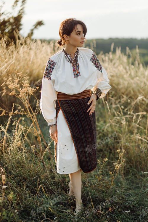 Preview: Young woman in traditional national embroidered shirt and skirt on nature at sunset.
