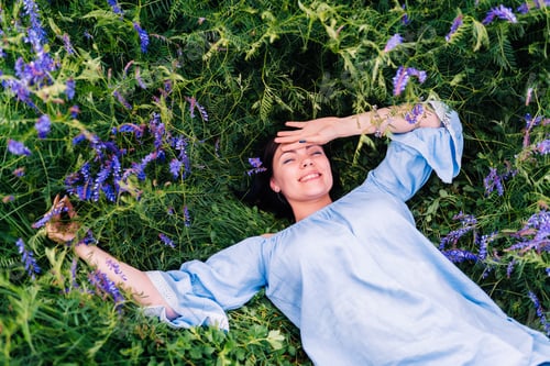 Preview: Happy smiling young woman falling down on grass with violet flowers