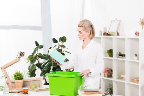 Preview: attractive woman holding milk package near recycling box while standing in office, environmental