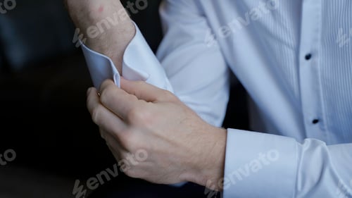 Preview: The man gets dressed and does his buttons on the sleeves of his white shirt. Action. Close up of