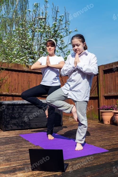 Preview: Happy Mother and Daughter are doing online yoga with laptop during self isolation at their back