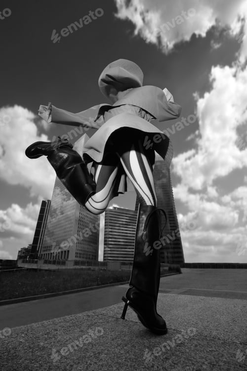 Preview: Vertical low-angle shot of a young female with heels jumping in front of a modern skyscraper