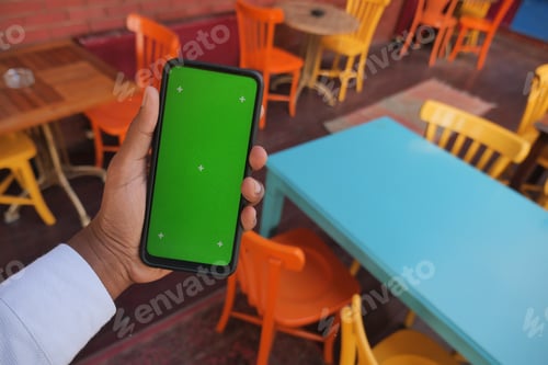 Preview: Hand holding a smartphone with a green screen in cafe