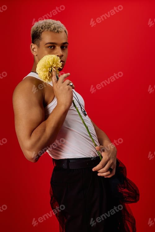 Preview: Young man in tank top and black pants poses stylishly in vibrant red studio