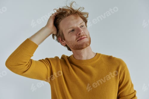 Preview: Handsome young redhead man holding hand in hair while standing against wall