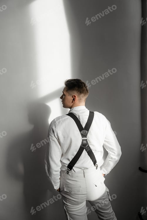 Preview: a young guy stands against the wall in a white shirt and black suspenders