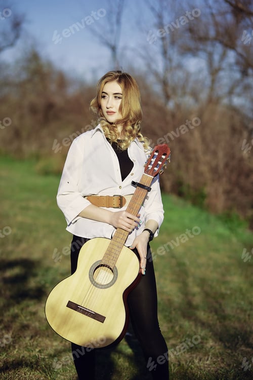 Preview: Beautiful girl playing guitar around spring sunny nature