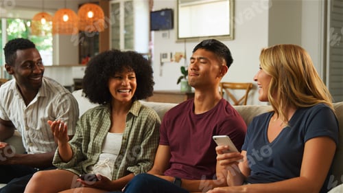 Preview: Friends Enjoying a Relaxing Evening Together at Home While Sharing Laughter and Using Mobile Phones