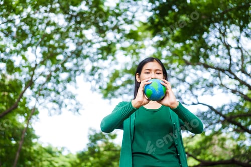 Preview: An Asian woman holds a globe in green forest,symbolizing importance preserving nature.emphasizes