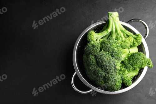 Preview: Fresh green broccoli in colander on black table, top view. Space for text