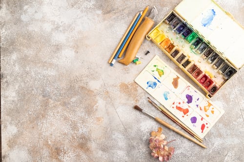 Preview: Drawing accessories set: brushes, pencils, watercolor on brown concrete. Top view, copy space