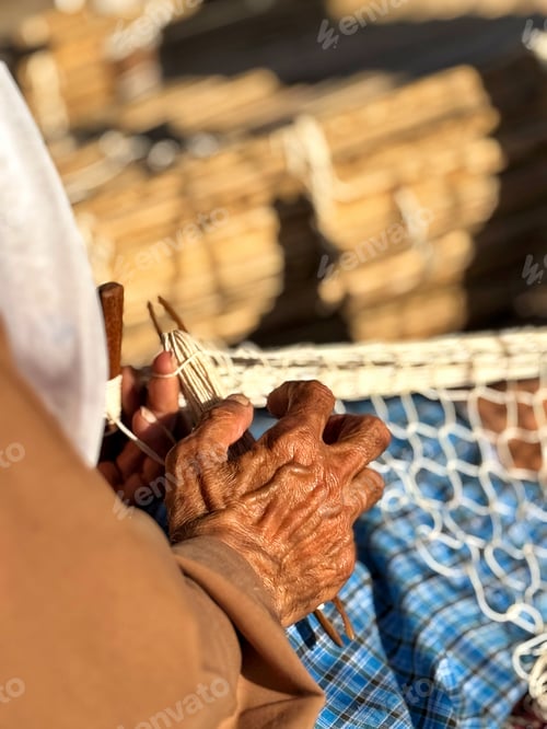 Preview: An unrecognizable elderly senior fisherman quietly mends his fishing net by hand alone by himself