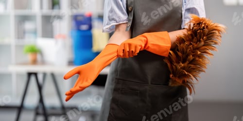 Preview: Female office cleaner putting on gloves with duster. Concept of workplace cleanliness