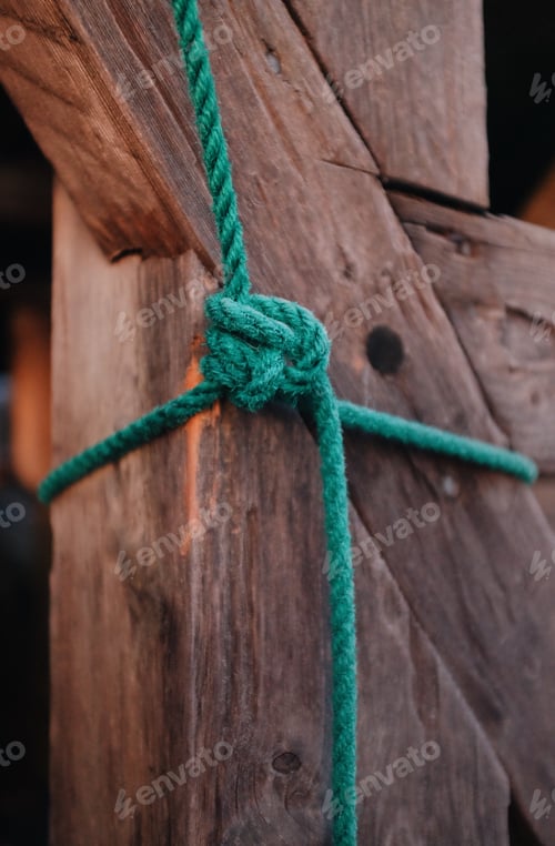 Preview: detail of a knot on a green rope tied around wooden timber