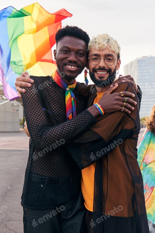 Preview: Cheerful portrait of gay couple hugging while looking at camera smiling celebrating the LGBTQ month.