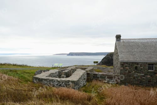 Preview: Horizontal shot of a grey stone house near a body of water with a grass field near it