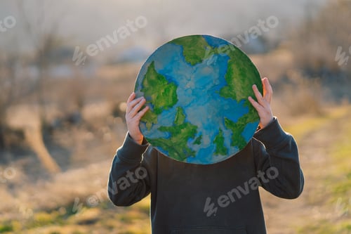 Preview: Little boy holding planet in hands against green spring background